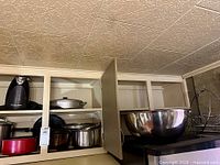 Overall cupboard view showing can opener, assorted cookware, mixing bowl and rack