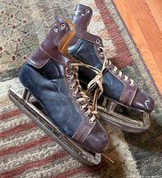 Overall view of pair of black and brown leather hockey skates with laces and blades