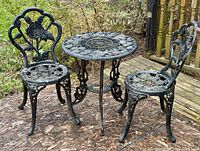 Full view of round cast-iron table and two matching chairs with rose motif