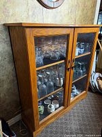 Front view of oak curio cabinet with glass doors and shelves holding glassware