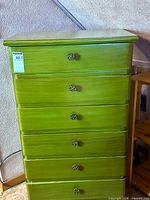 Full front view of green tallboy dresser showing five drawers and knobs