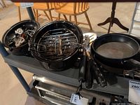 two enamel roasting pans with turkey lifter, frypans and BBQ tools on shelf