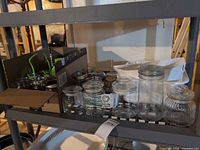 Shelf section with mixed glass canning jars, green funnel and jar lifter visible