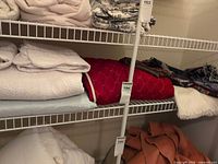 Shelved bedding showing burgundy bedspread, pale green bedspread beneath, off-white fringed throw and multicolour woven throw