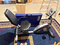 Side view of Exerpeutic recumbent bike with blue tri-fold mat beside it