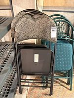 Two black metal folding chairs with grey patterned fabric folded against shelving