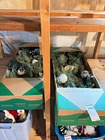 Two cardboard boxes containing evergreen garlands on shelf
