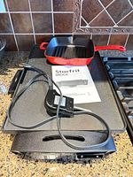 Starfrit electric griddle with cord, manual, and Lava grill pan displayed on top