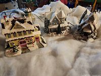Three snow-covered lighted village buildings with cords