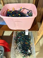 Two bins with tangled Christmas light strings, pink bin above clear bin