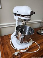 White KitchenAid Professional stand mixer with stainless bowl attached on wooden surface