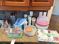 Countertop view of all plastic containers, pitchers, cake carrier, tablecloths