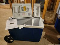 Open view of blue wheeled thermoelectric cooler showing interior divider, lid module, manual
