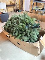 Artificial Christmas tree branches and pole inside damaged cardboard box