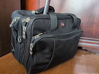 Front view showing zip compartments, fabric handles, telescopic handle shaft