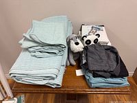 Stack of aqua quilted coverlets with plush toys and folded fabrics