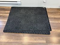 two stacked dark grey rectangular doormats on wooden floor