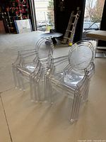 Six clear acrylic ghost-style armchairs stacked in two groups