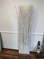 Full view of tall white painted willow bundle leaning against wall