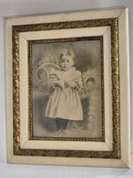 Framed antique sepia photograph of young child with cream and gold ornate frame