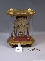 Full view of gilt and glass Schmid musical mantel clock with key in foreground
