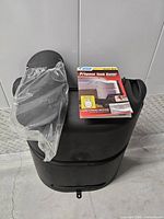 Cover standing upright with lid in plastic and instruction booklet on top