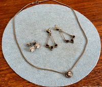 All three jewelry pieces laid out: pendant necklace, geometric drop earrings, CZ stud earrings