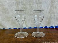 Front view of both matching clear ribbed glass bud vases on wood surface