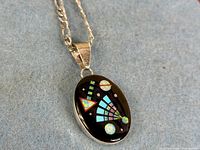Front view of sterling oval pendant showing multicolour geometric inlay on black stone and attached Figaro chain