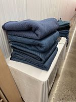 Stack of four folded dark blue moving blankets on table
