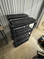 Two black plastic shelving units stacked together showing four vented shelf platforms each