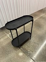 Full view of black two-tier oval side table showing frame and both shelves