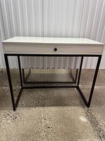 Front view of desk showing white top, drawer, black metal base