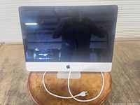 Front view of iMac showing 21.5-inch screen, Apple logo, power cord on table