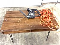 Hedge trimmer with coiled orange extension cord on table