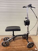 Side view of entire knee scooter showing frame, wheels, handlebar, brake cable, cup holder