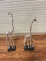Both giraffe sculptures side by side on wooden surface