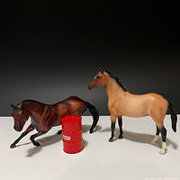 Both Breyer model horses and red barrel on white surface