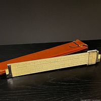 Slide rule beside brown leather case, full view