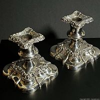 Front view of both silver plated candlesticks showing ornate detachable tops and square bases
