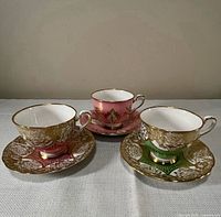 Front view of three teacup-saucer sets showing colours and gilt pattern