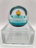 Front view of spherical crystal paperweight on clear stand showing amber orb, teal ground, frosted bubble crown and etched star