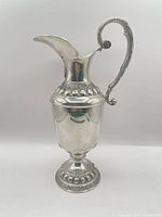 Side view of ornate pewter pitcher showing scroll handle and pedestal base