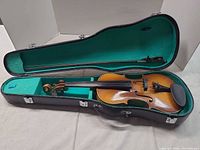 Violin inside open green-lined hard case with bow and shoulder rest visible