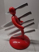Side view of red human-figure knife stand holding five stainless steel knives