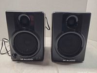 Front view of both speakers showing grilles, tweeters, controls and branding