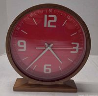 Front view of clock showing red face, numerals, wood base
