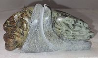 Left side view showing green and brown marbled carving with overlapping face forms