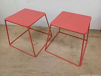 Pair of red metal stools side by side on wood floor, showing tops and frames