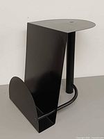 Three-quarter view of black metal end table with integrated magazine holder